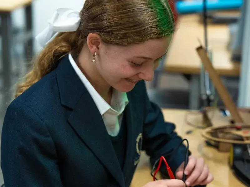 Estudiante de secundaria realiza experimento científico con cables en laboratorio escolar